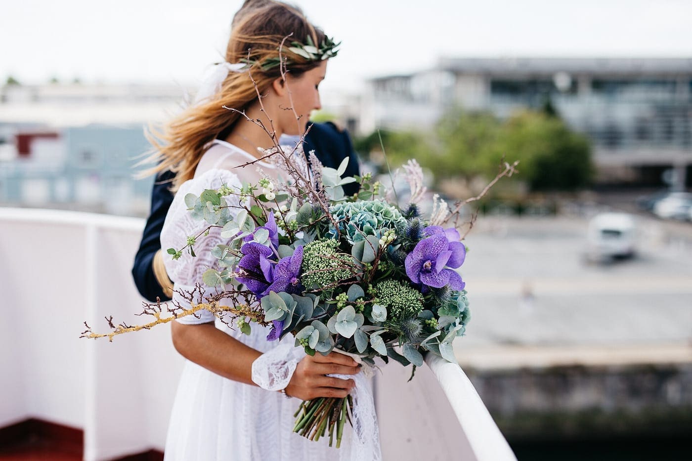 A bride holding a large bouquet of eucalyptus, succulents and purple anemones.