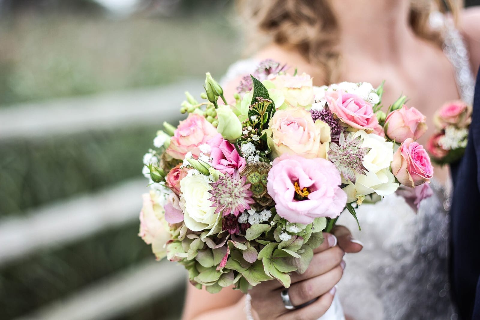 A garden-style bouquet of pink roses, lisianthus, astrantia and hydrangea held by a bride.
