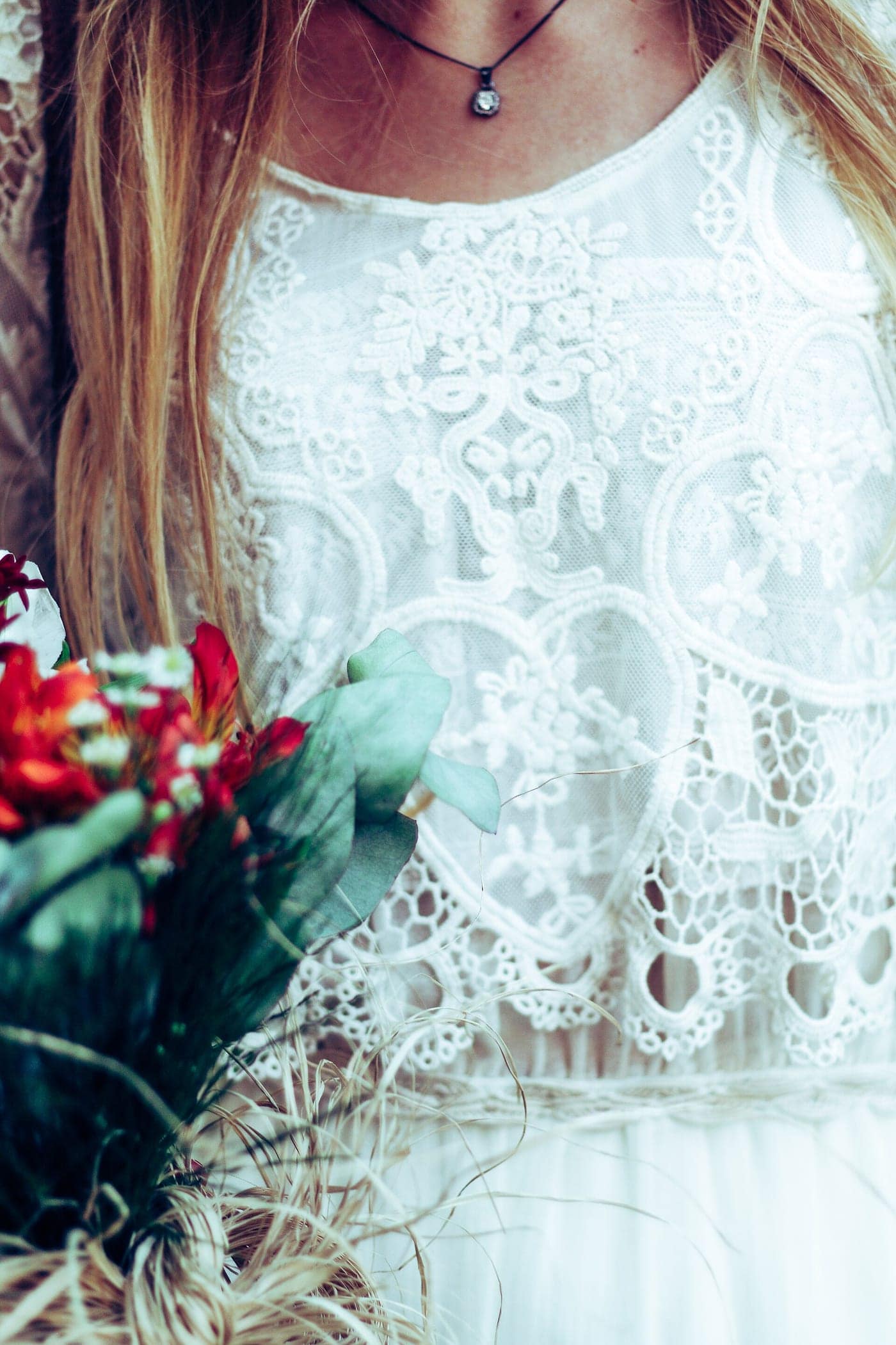 Red and orange blooms with eucalyptus and dried grasses held against a lace dress.