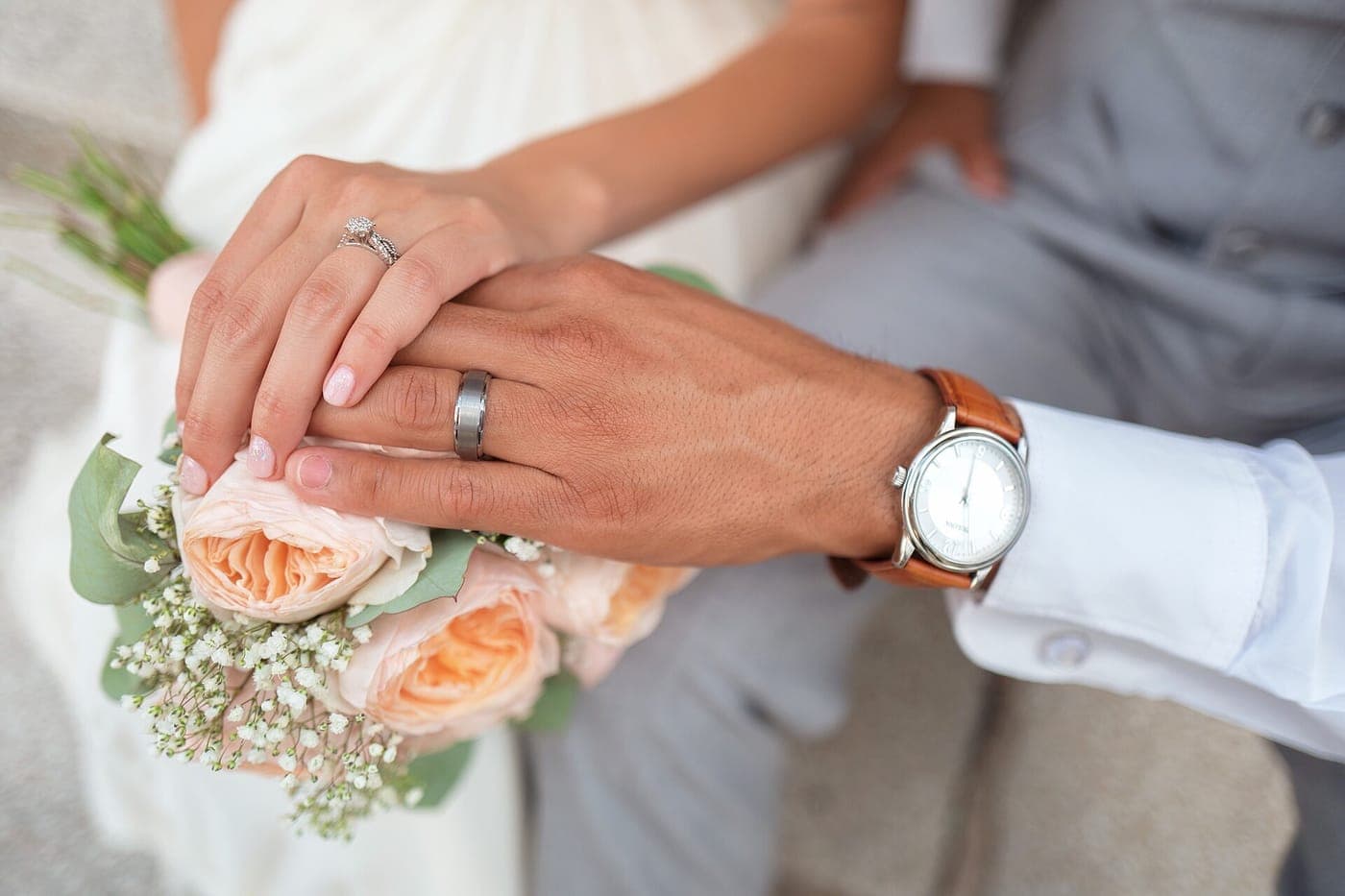 A couple's hands with wedding rings resting on peach garden roses.